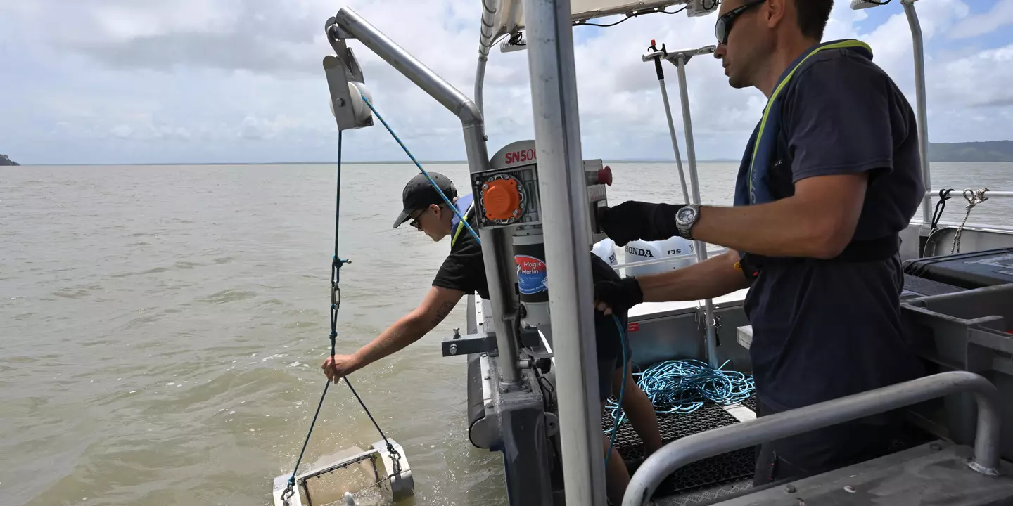 Deux personnes à bord d'un bateau qui mettent à l'eau un engin.