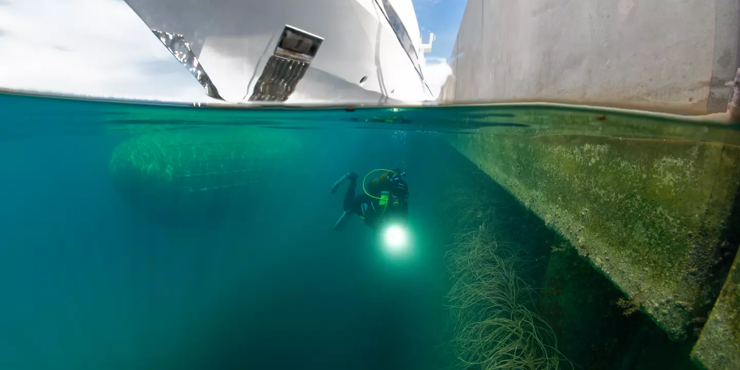 Prise de vue au ras de l'eau d'un plongeur entre un bateau et une digue.