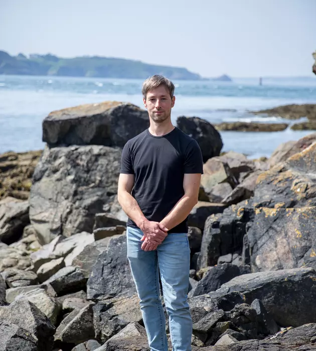 Homme debout sur des rochers en bord de mer.