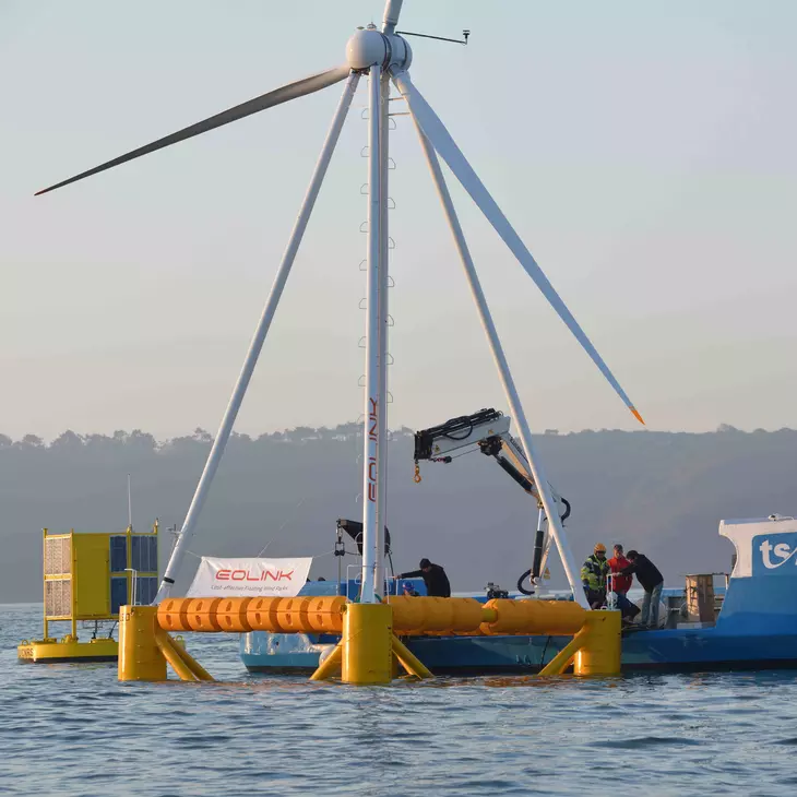 Bateau à moteur derrière une éolienne marine avec plusieurs personnes à son bord