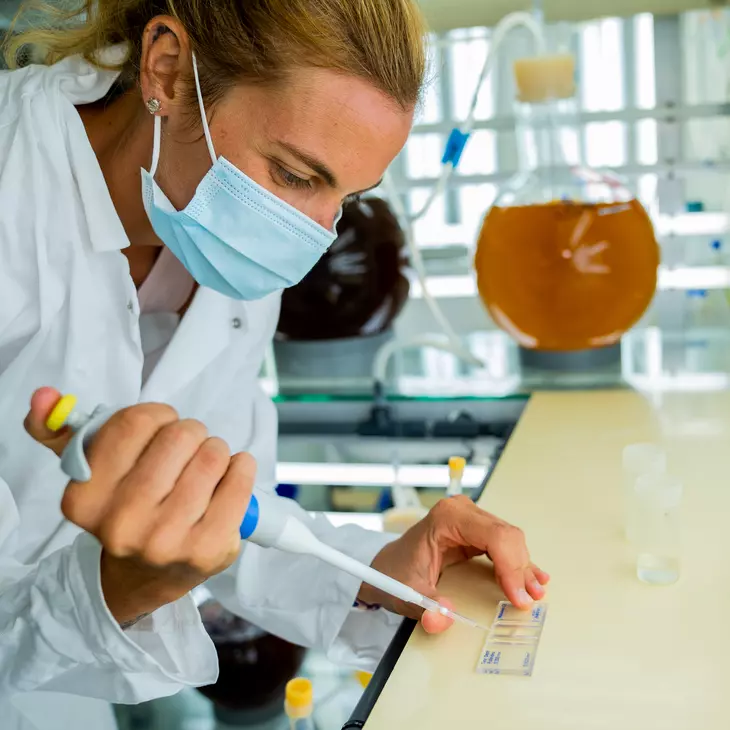 Personne en blouse blanche manipulant des éléments techniques en laboratoire.